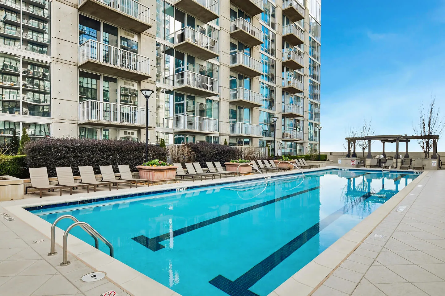 Resort-style pool with lounge chairs and a covered grilling area at a high-rise residential building